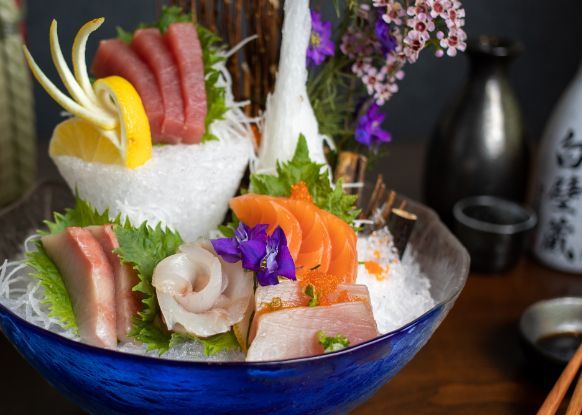 A bowl of sashimi with ice and chopsticks on a table.