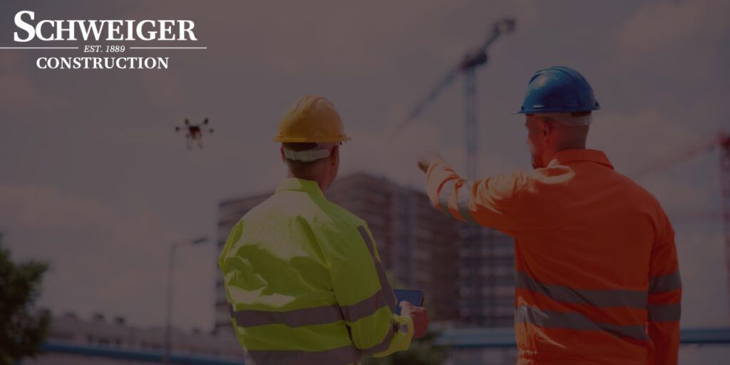 Two construction workers are looking at a drone on a construction site.