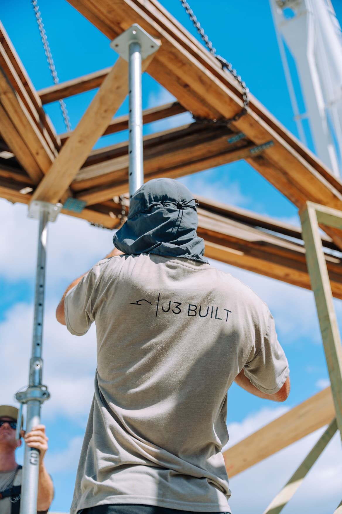 Construction worker using a support pole, working on a wooden structure under a blue sky.