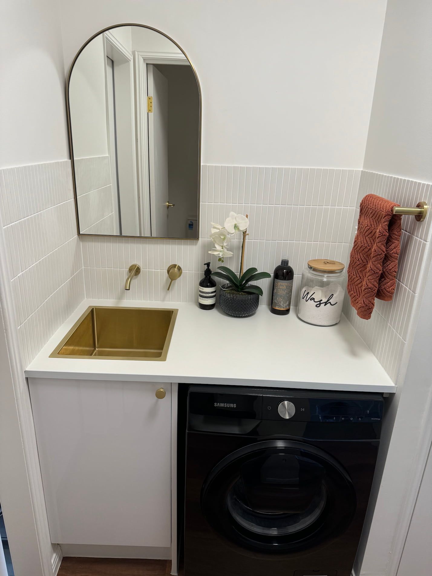 A laundry room with a washing machine , sink and mirror.