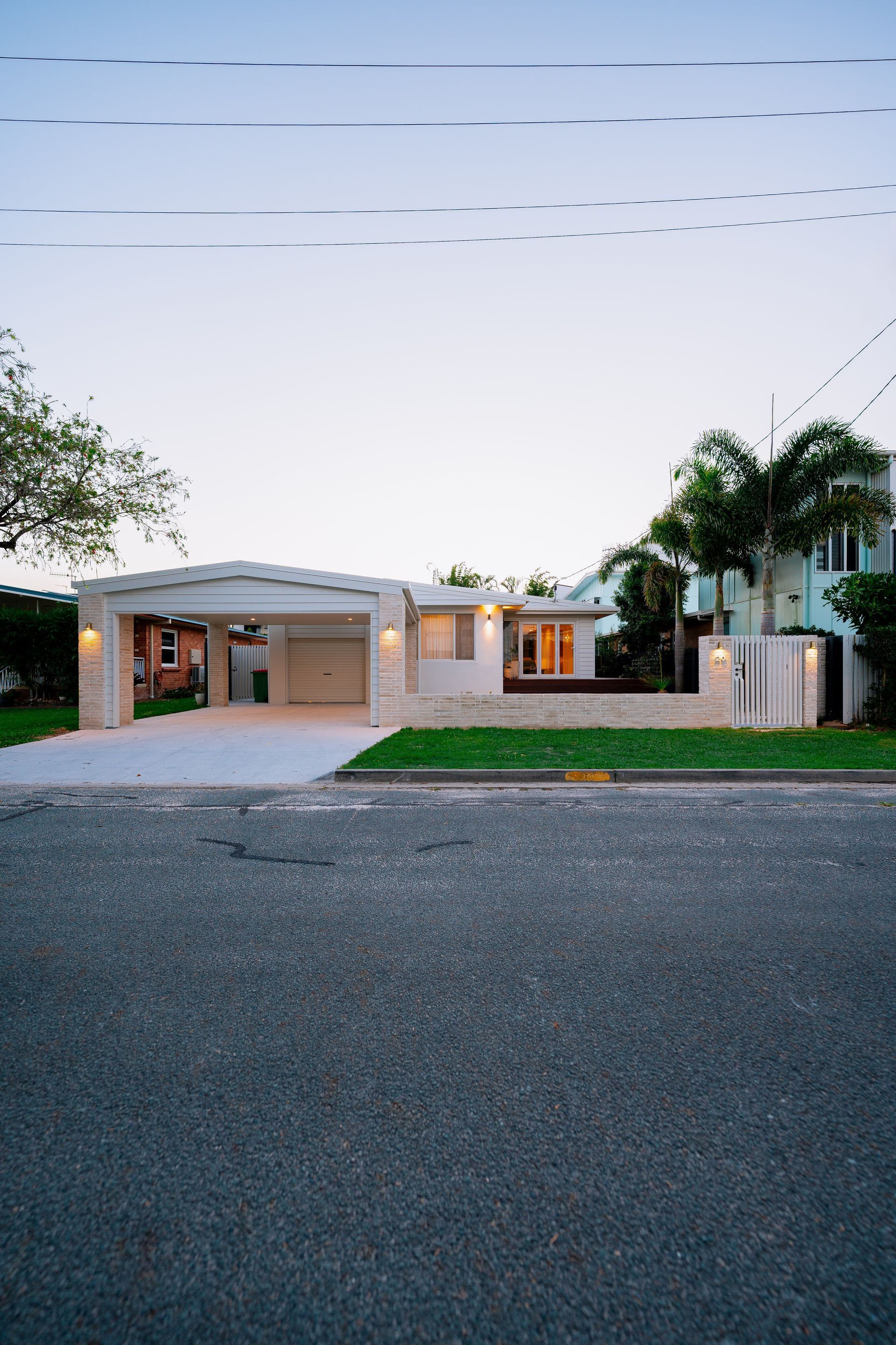 A modern white house with a carport and green lawn against a colorful sky.