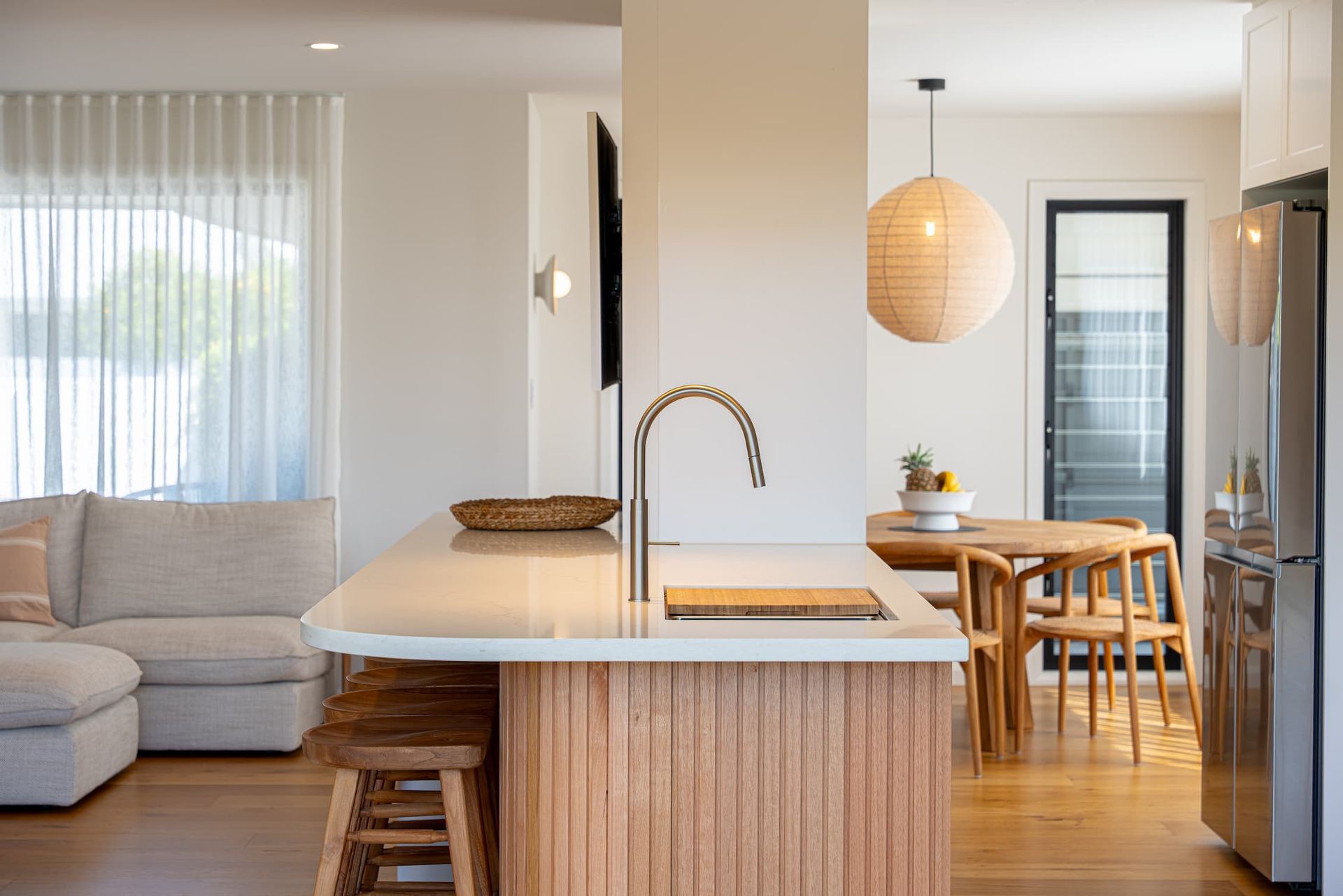 Modern kitchen with wooden island, dining table, and living area with white walls and natural light.