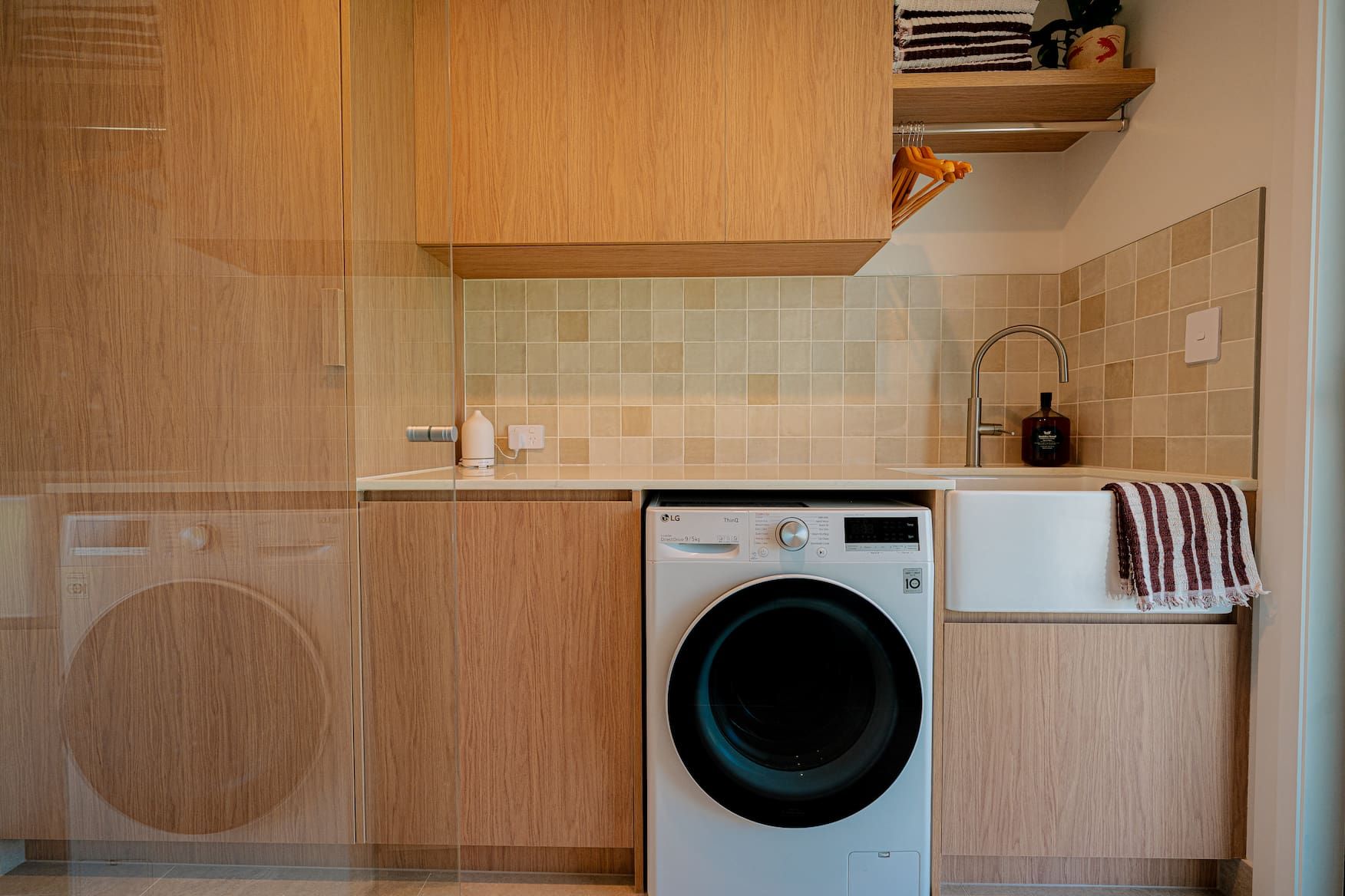 Laundry room with light wood cabinets, white washing machine, and farmhouse sink.