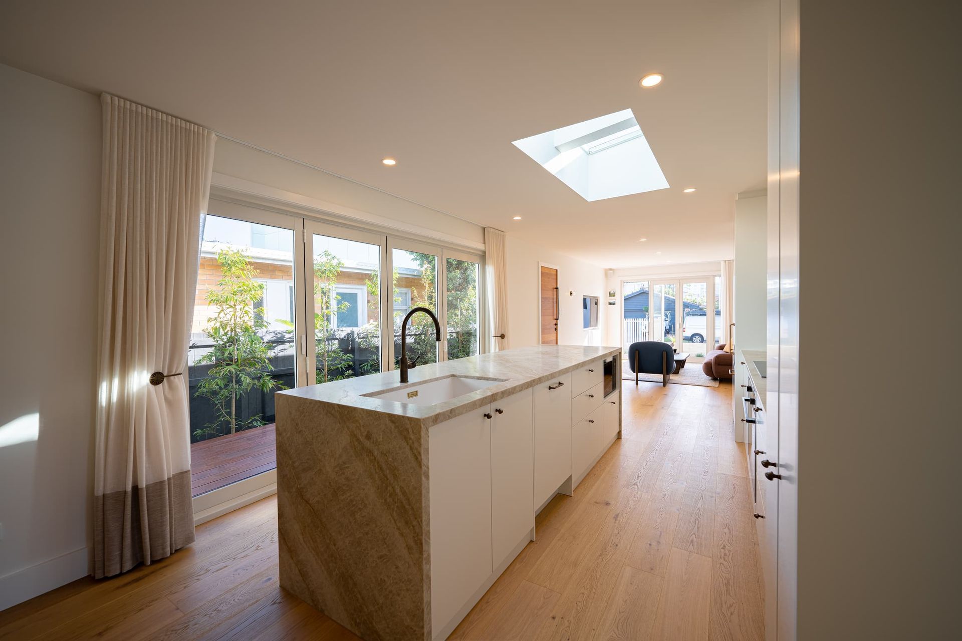 Bright kitchen with island, skylight, and open doors leading to a patio.