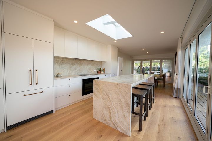 Modern kitchen with white cabinets, marble counters, and wood floors.