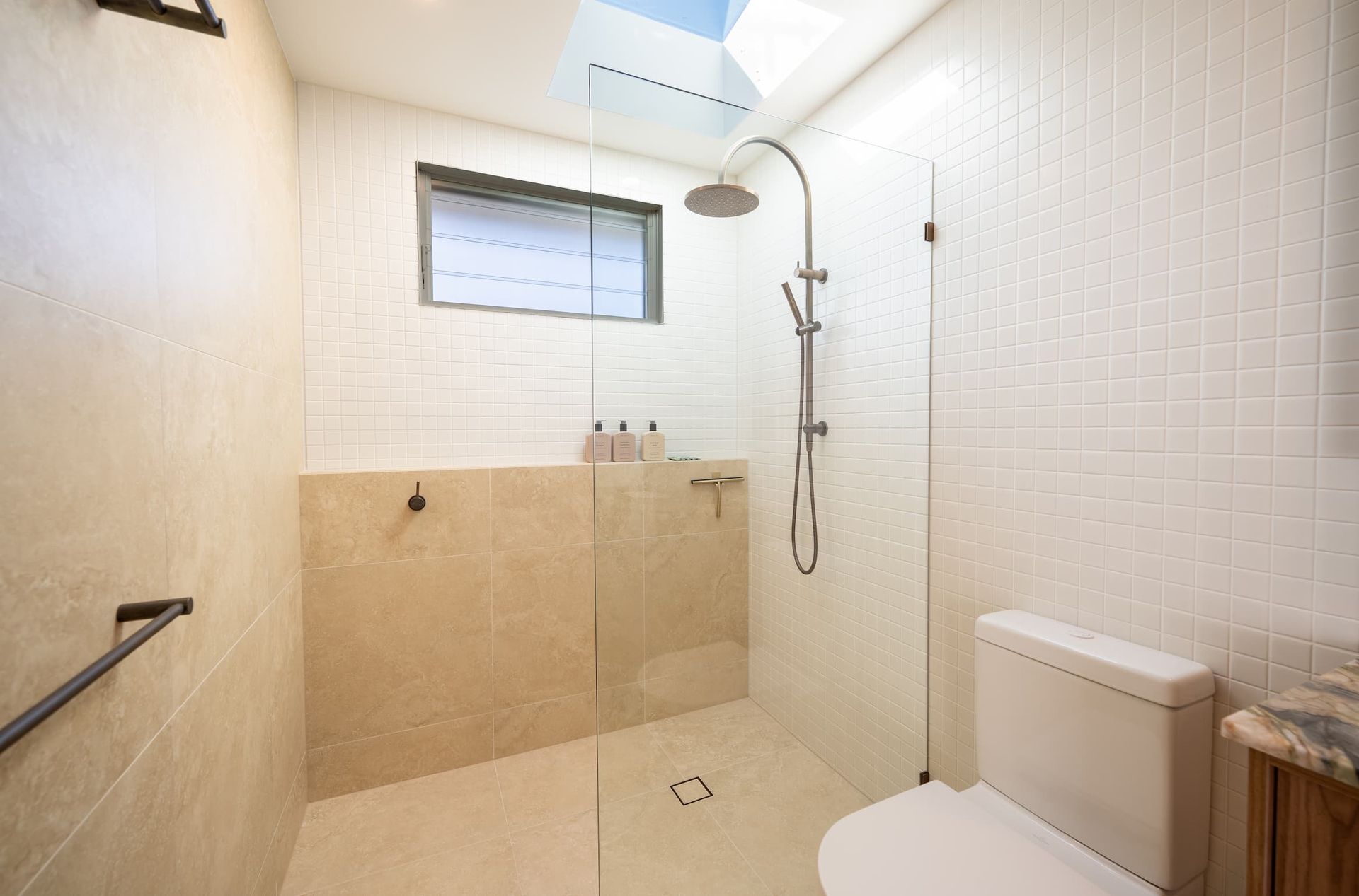 Modern bathroom with white and beige tile, glass shower, and toilet.