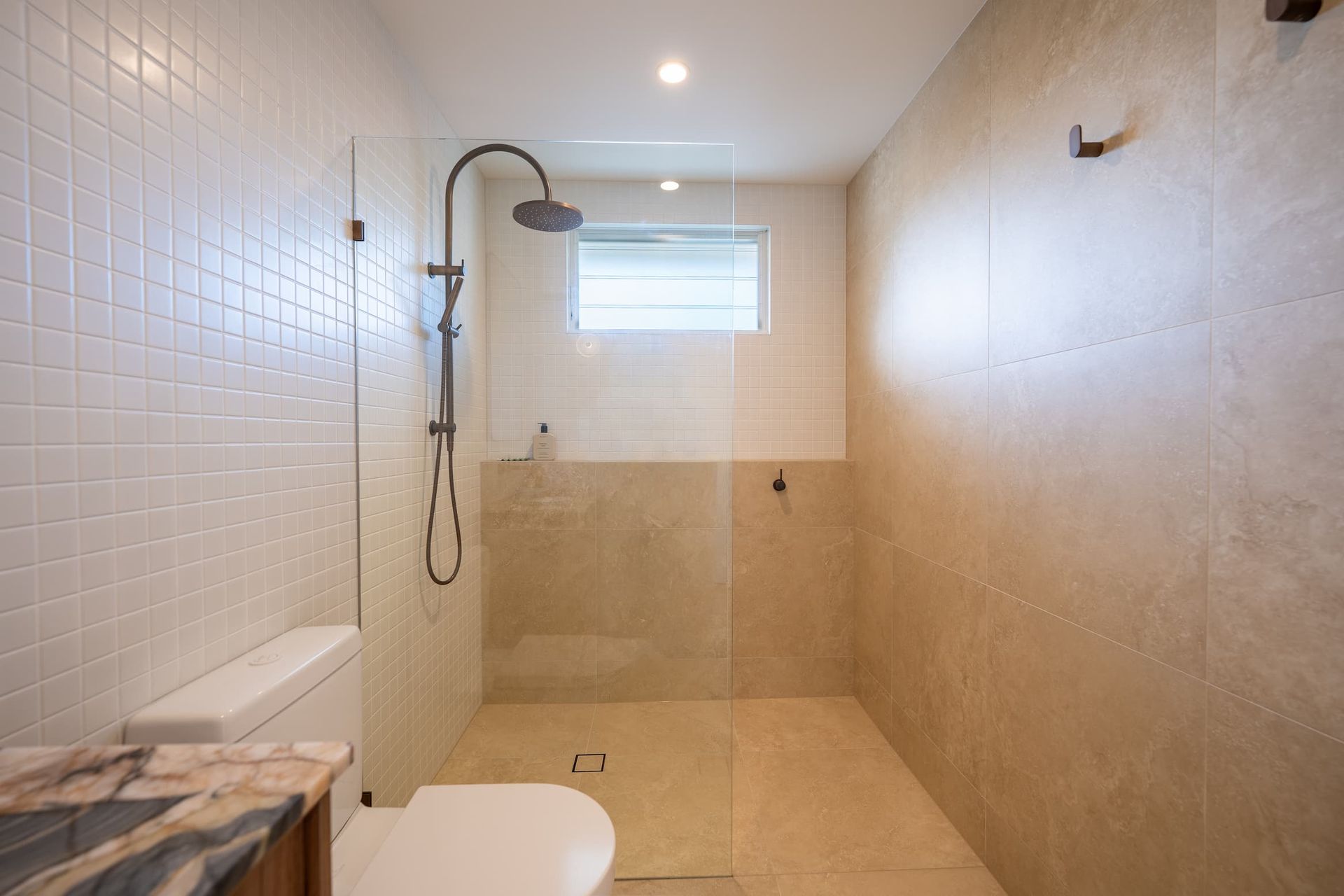 Bathroom with white tiled walls, a glass shower, toilet, and beige tiled walls.