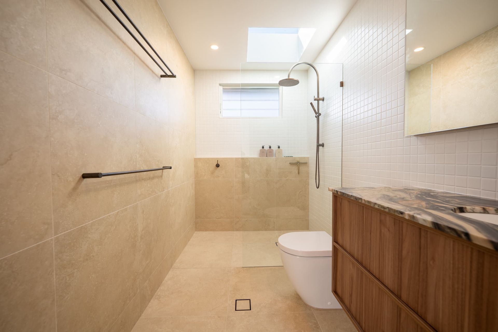 Modern bathroom with beige and white tiles, wooden vanity, and a skylight.