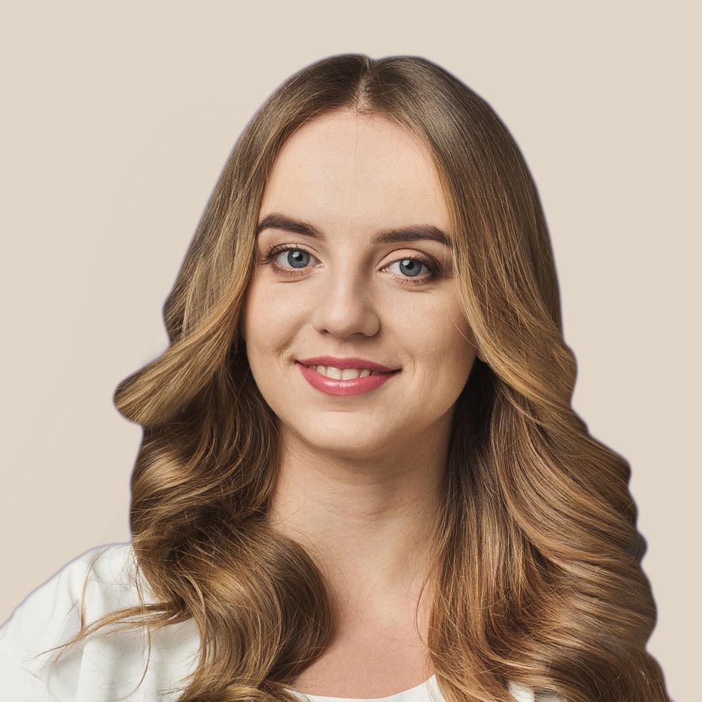 A woman with long brown hair is smiling and wearing a white shirt.