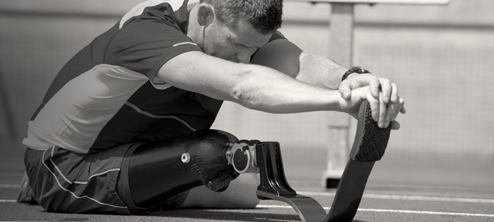 An above the knee amputee with a 3s80 knee joint is sitting on the floor stretching his legs.