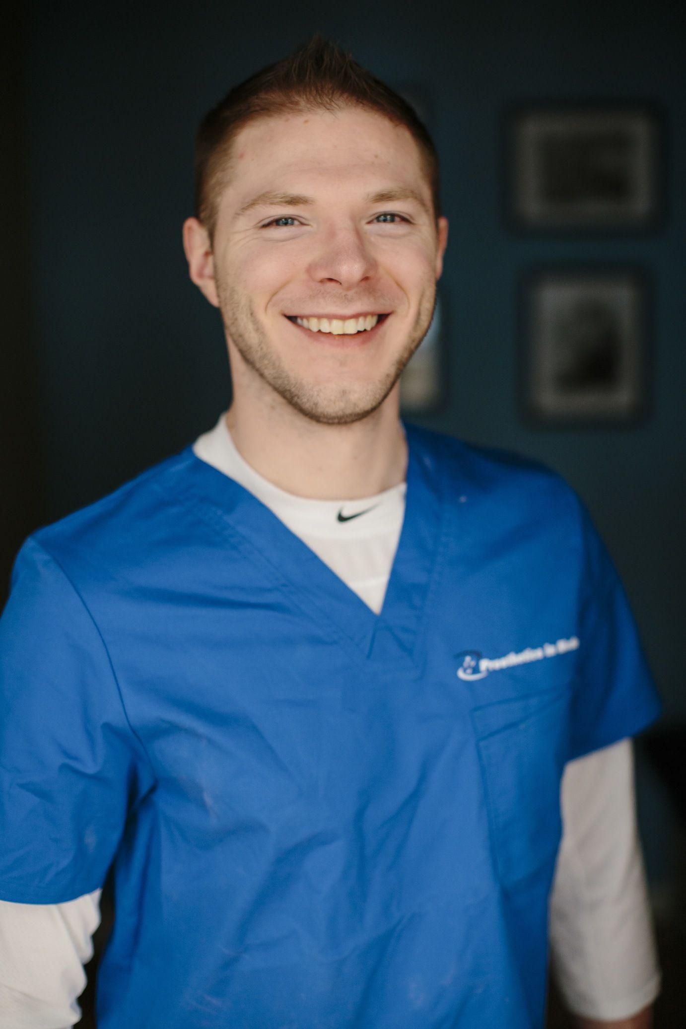 A man in a blue scrub top is smiling for the camera.