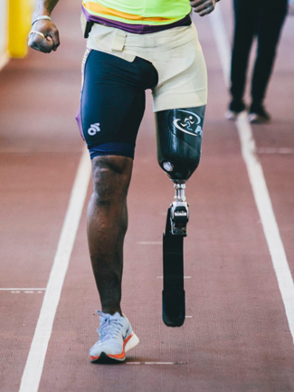 A person with an above the knee prosthetic running blade is running on a track.