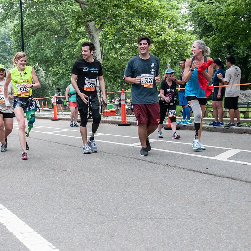 A group of amputees are running and walking  are walking down a street in the achilles hope and possibility race