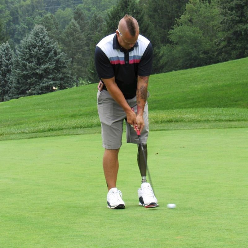 A man with a prosthetic leg is putting a golf ball