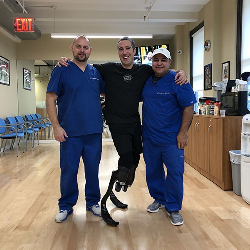 Three men in blue scrubs are posing for a picture in front of an exit sign