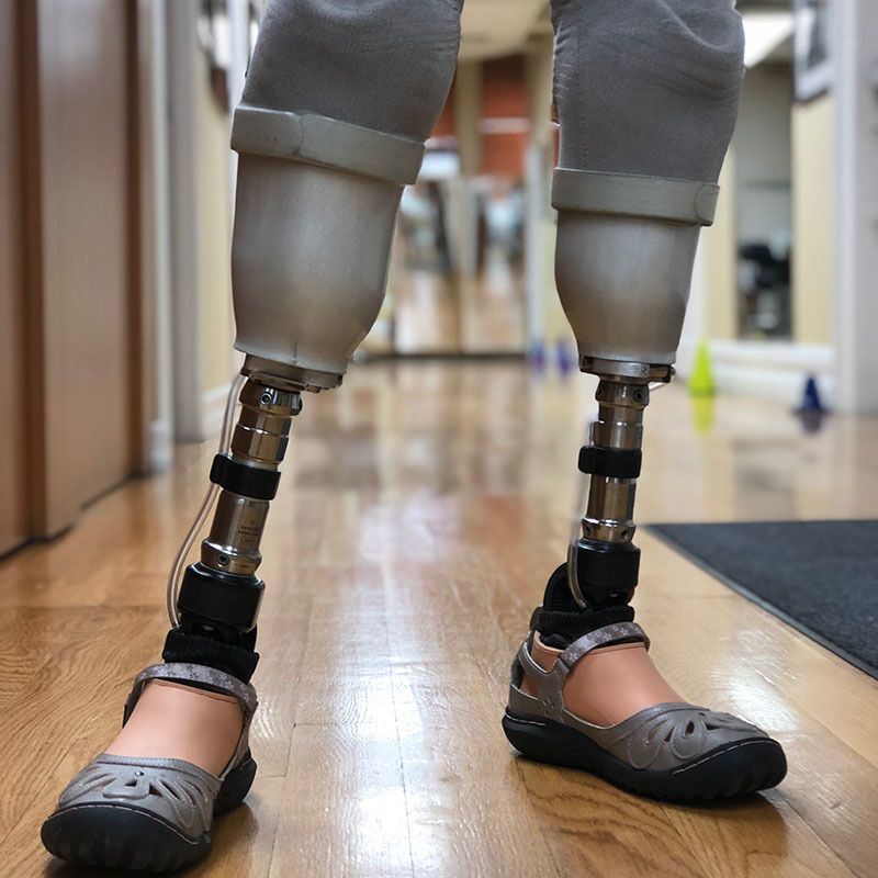 A person with prosthetic legs is standing on a wooden floor