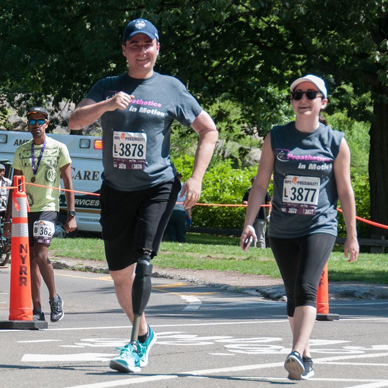A man with a prosthetic leg is running with a woman wearing a shirt that says l3877