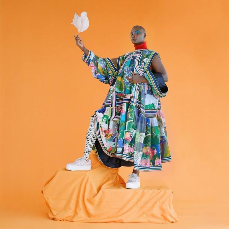 A woman in a colorful dress is standing on a stool holding a feather.