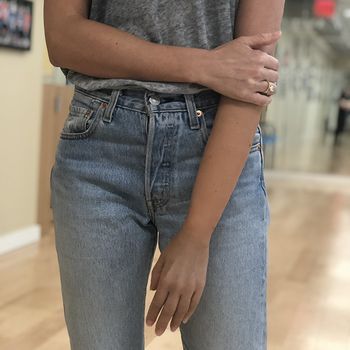 A woman wearing a gray shirt and blue jeans is standing with her arms crossed.