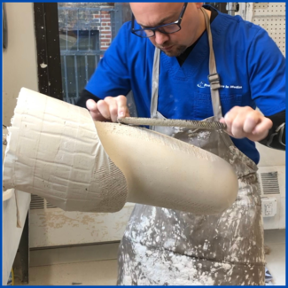A man in a blue shirt is working on a piece of clay