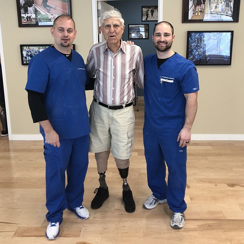 A man with a prosthetic leg poses with two men in blue scrubs