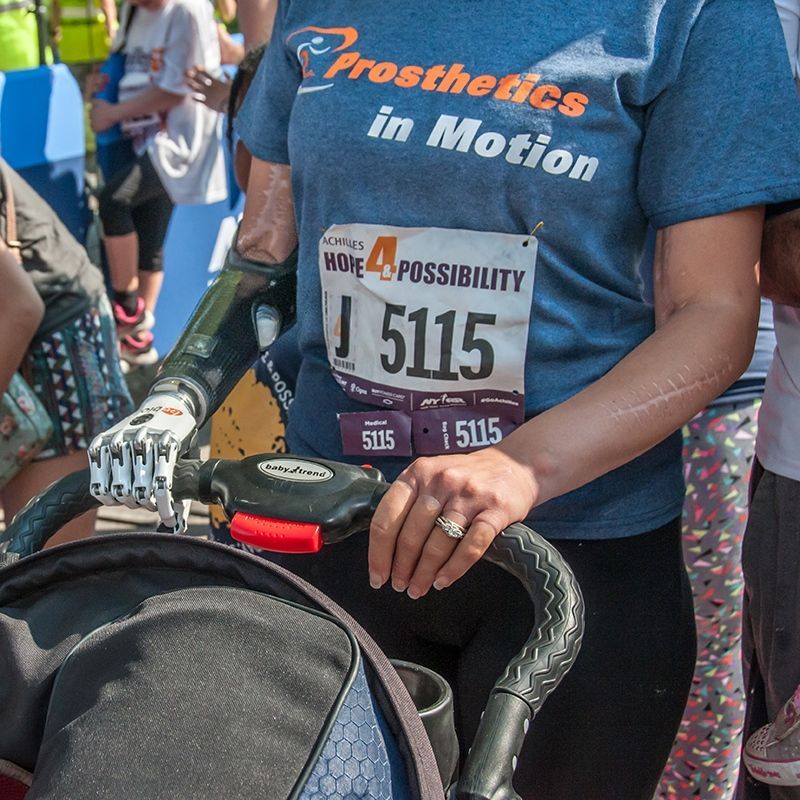A woman wearing a prosthetics in motion shirt is pushing a stroller