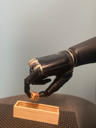 A robotic hand is reaching for a dice in a wooden box