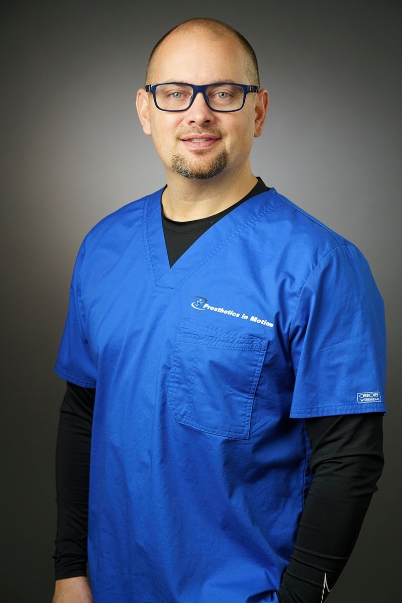 A man wearing glasses and a blue scrub top is posing for a picture.