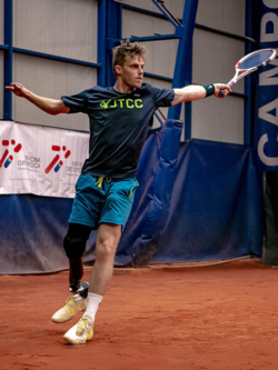 A man in a jtcc shirt is swinging a tennis racquet