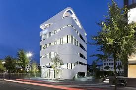 A large white building is sitting on the corner of a street at night.