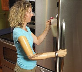 A woman with a prosthetic arm is opening the door of a refrigerator.