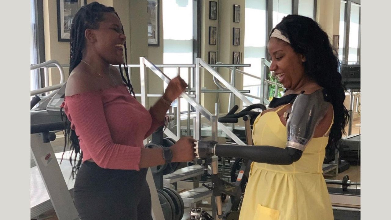 Two women are standing next to each other in a gym . one of the women has a prosthetic arm.