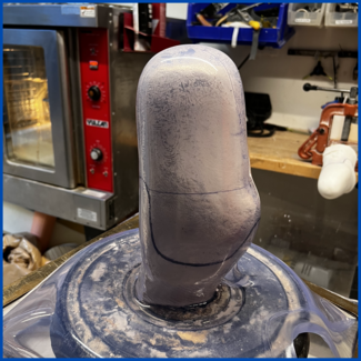 A gray object is sitting on top of a clear container with a red oven in the background