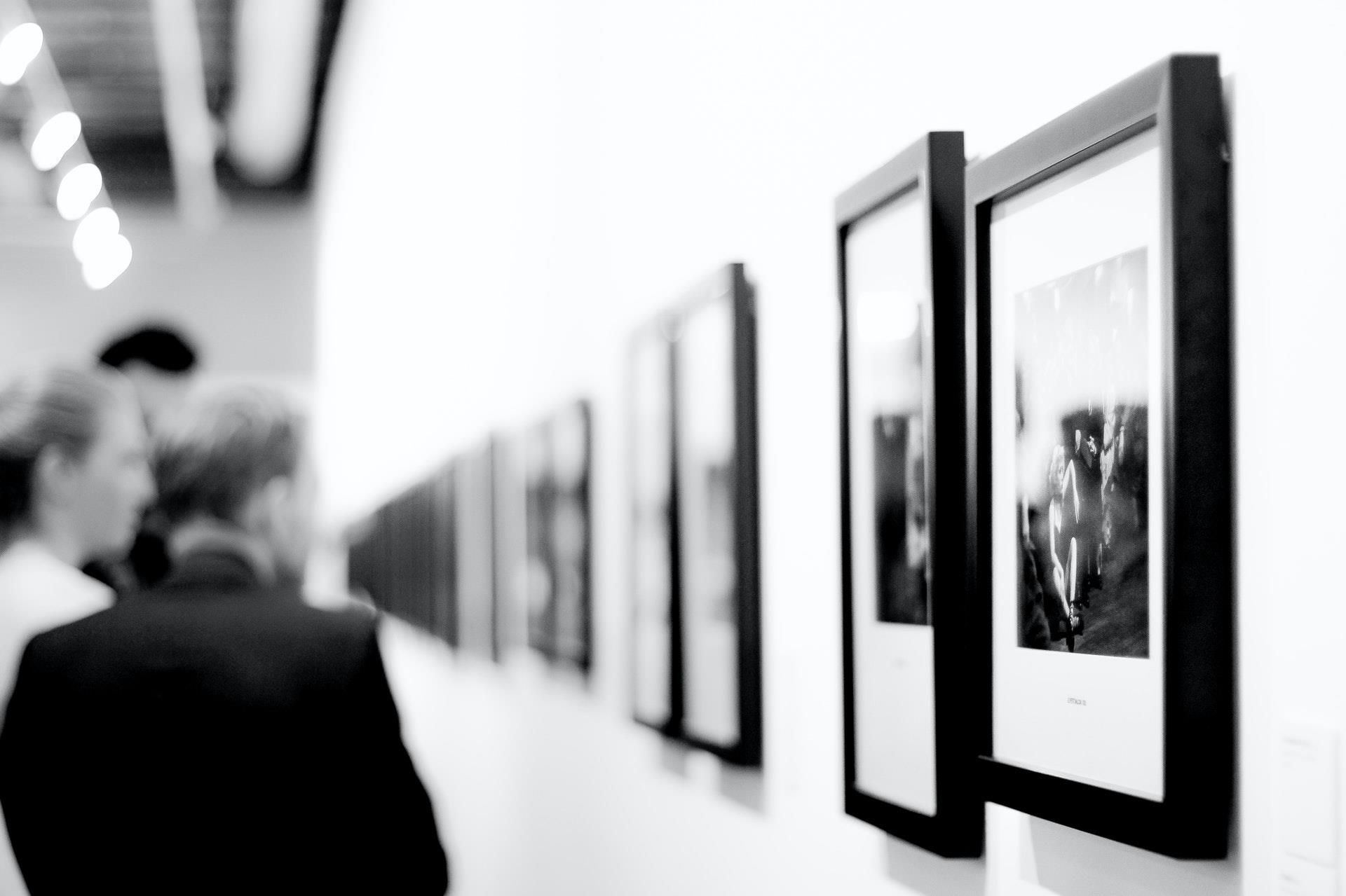 A black and white photo of people looking at pictures on a wall.