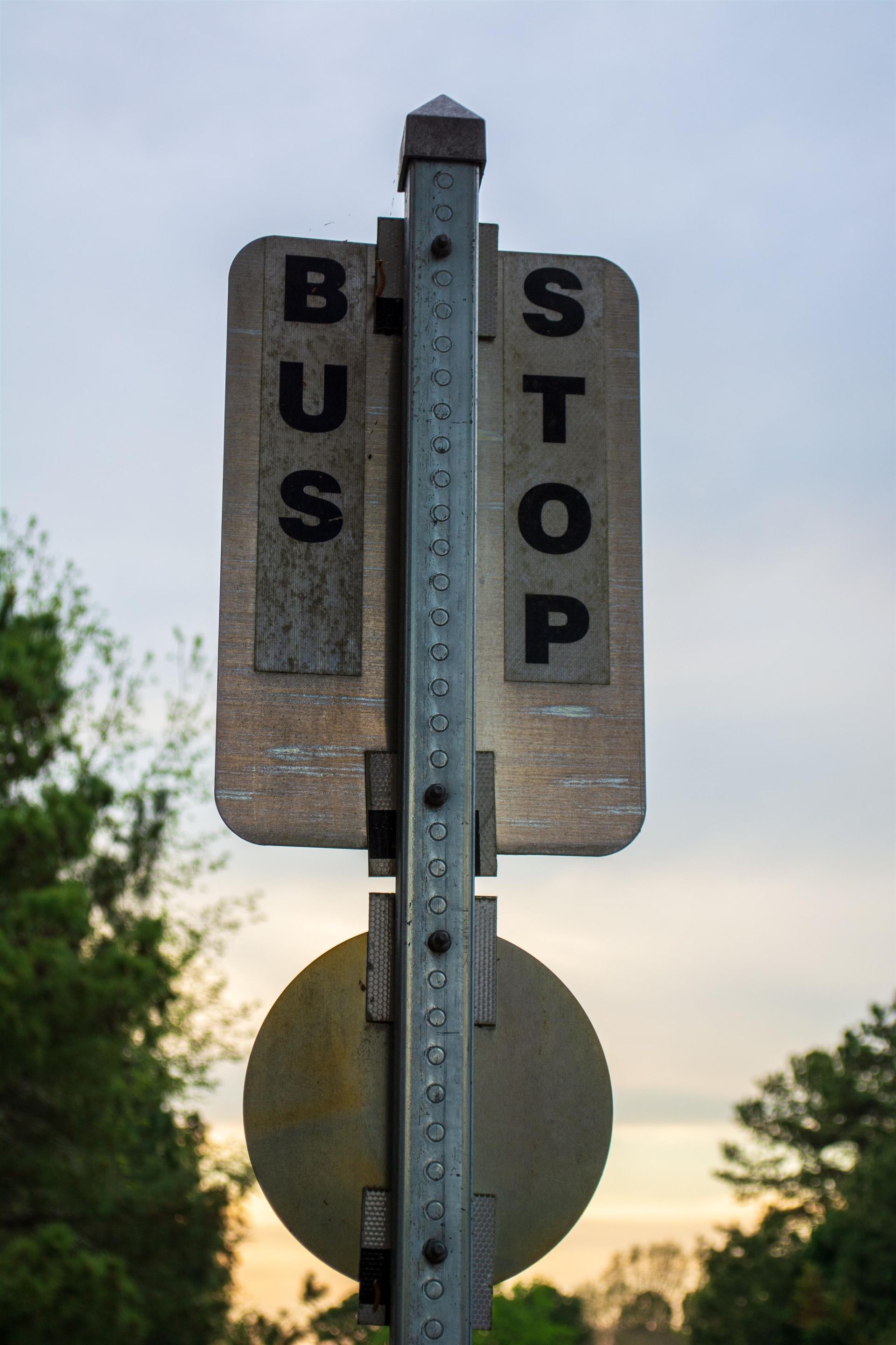 A bus stop sign is sitting on top of a metal pole.