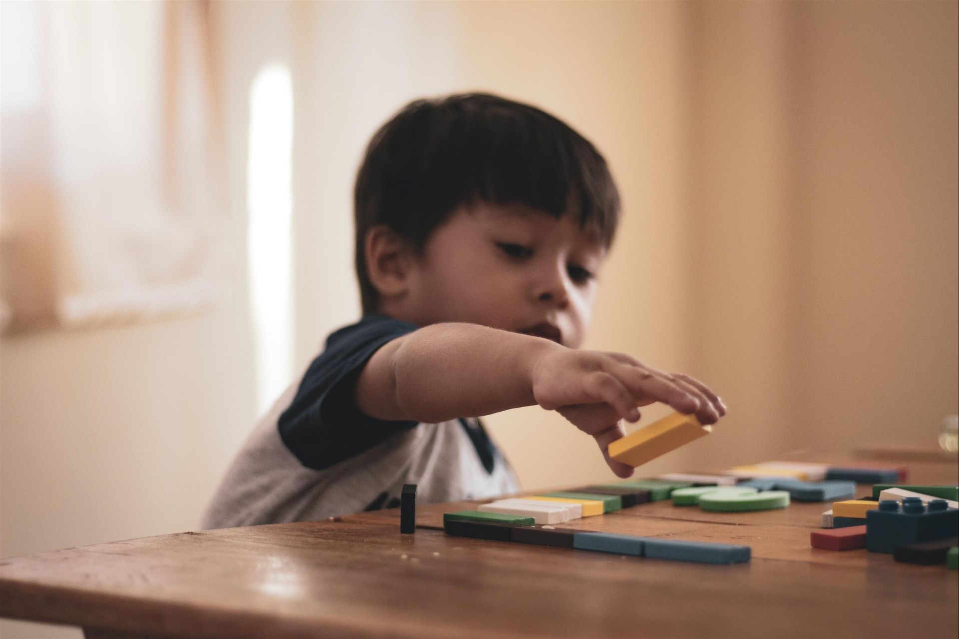 A young boy is playing with wooden blocks on a wooden table.
