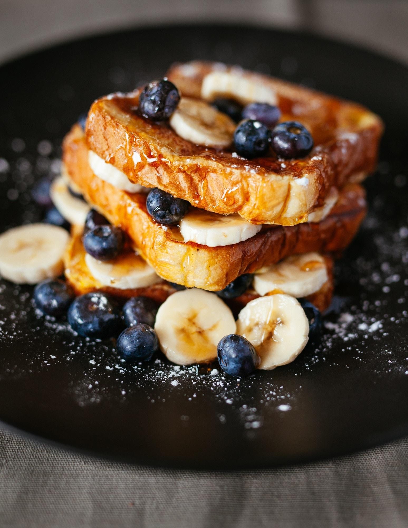 French toast with bananas and blueberries on a black plate