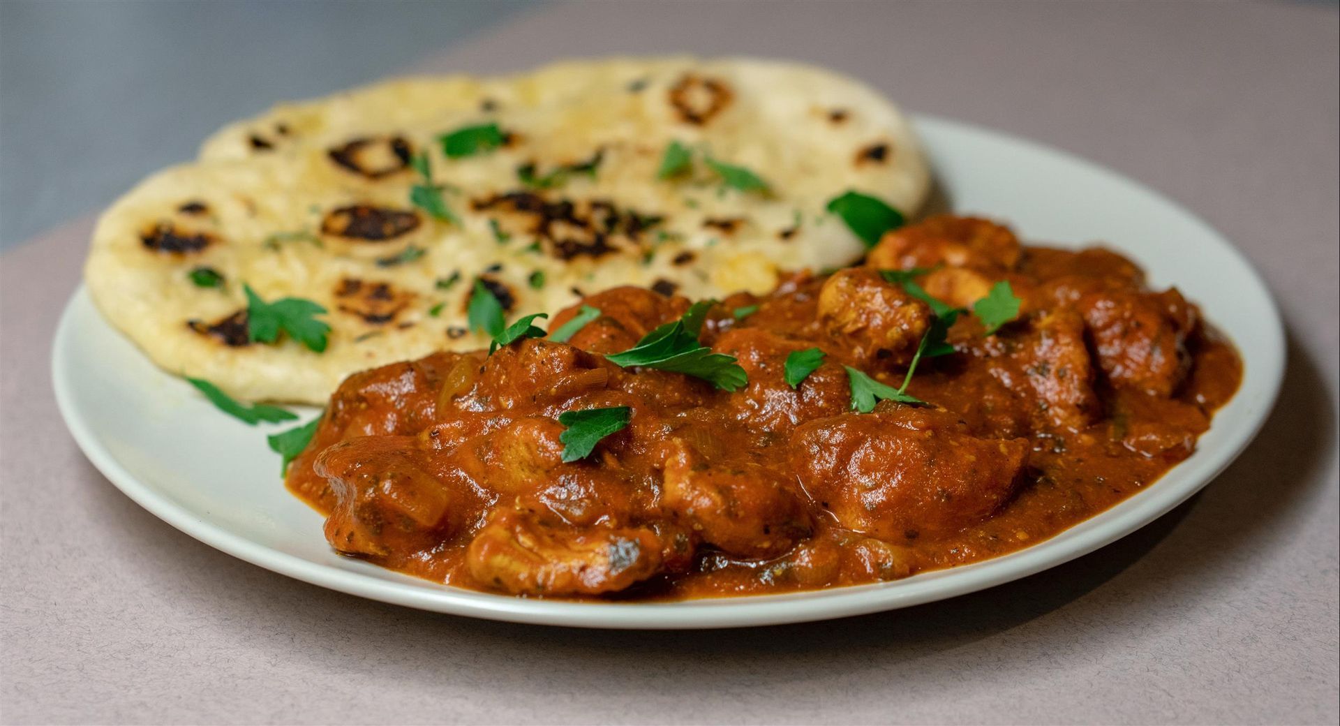 A white plate topped with chicken curry and naan bread.