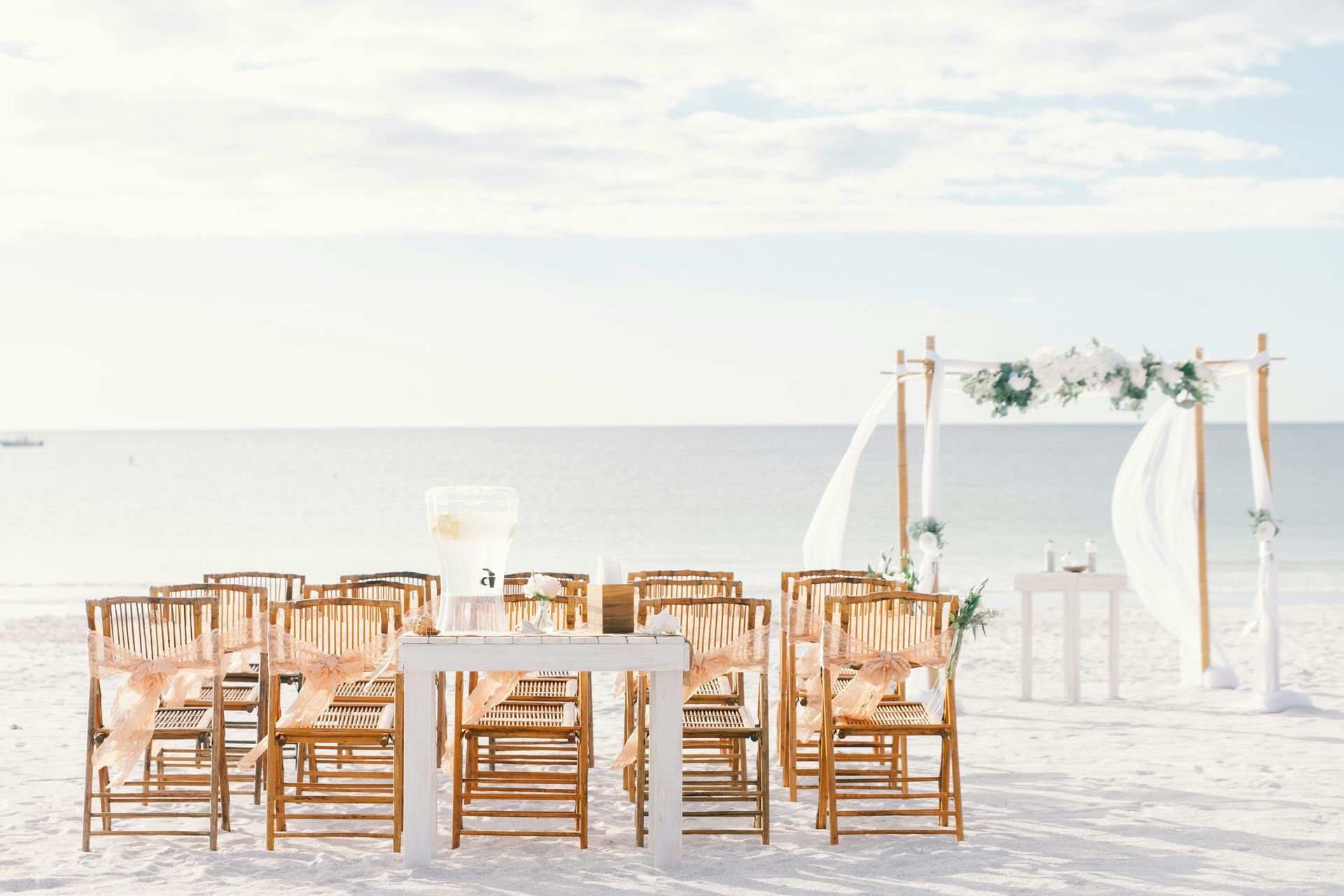 Beach wedding setup with chairs facing an archway on the sand, with ocean in the background.