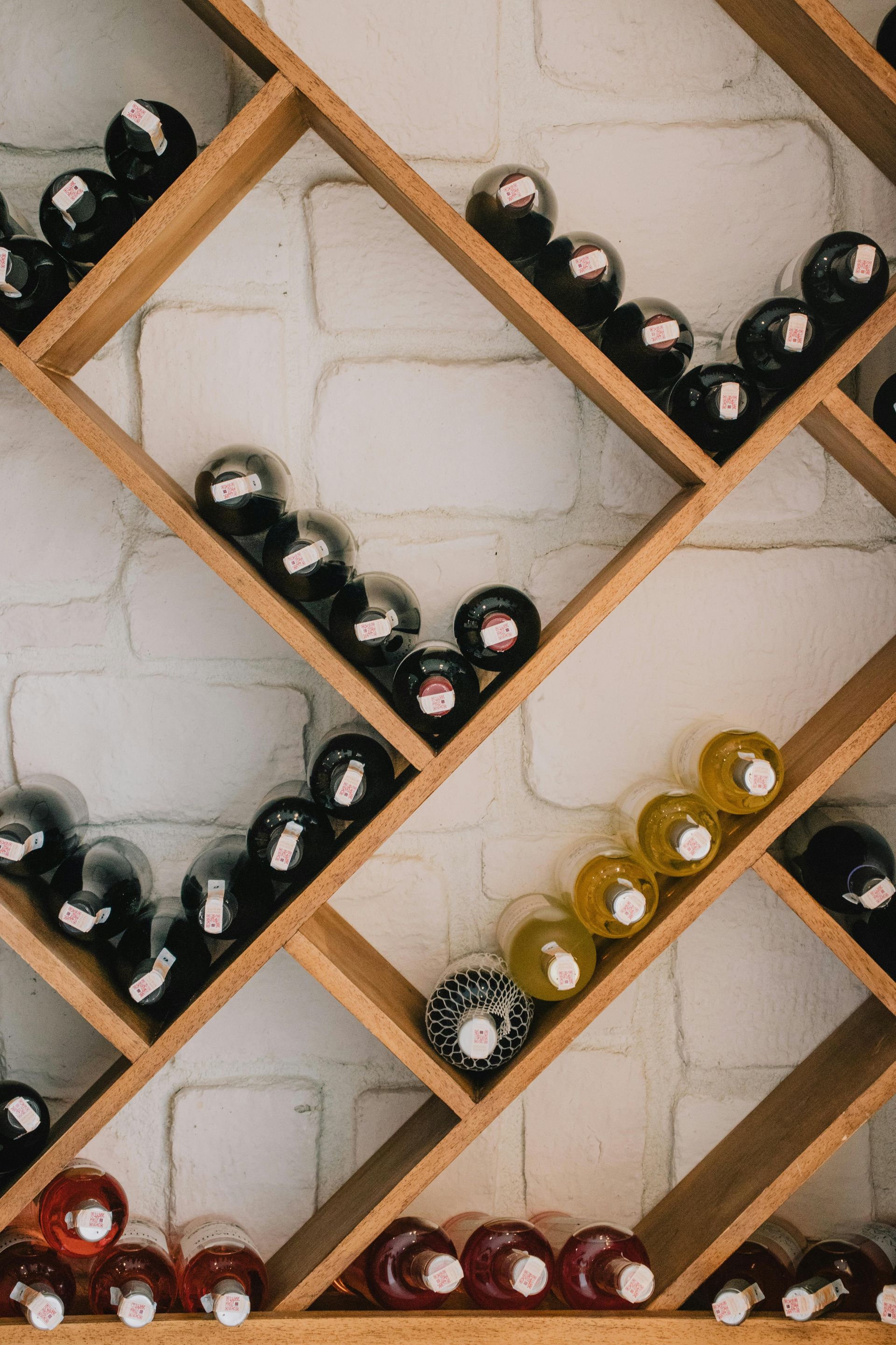 Wine bottles stored in a wooden rack against a white brick wall.