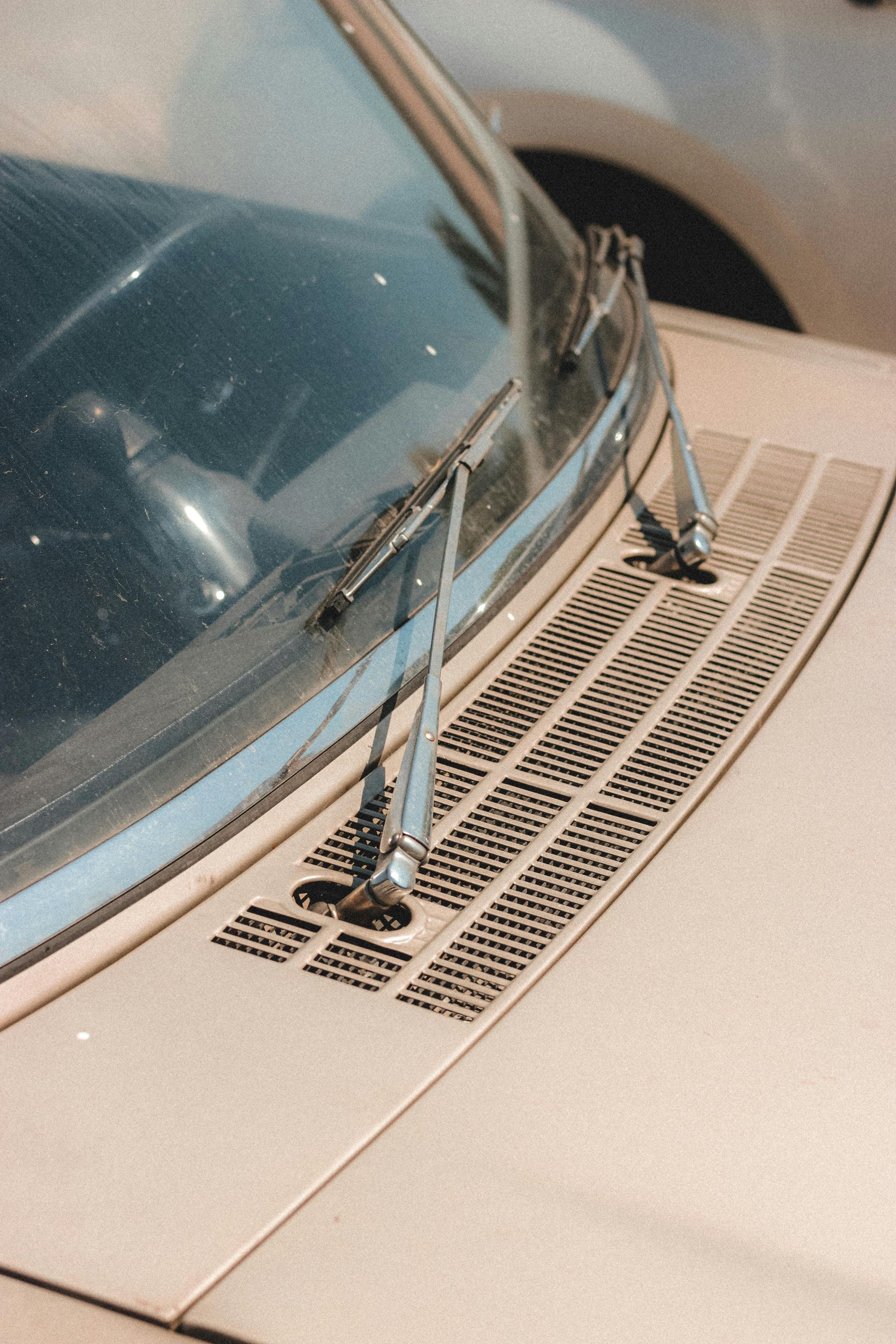 Close-up of a car windshield and wipers on a beige hood, with a vented grille near the base of the glass