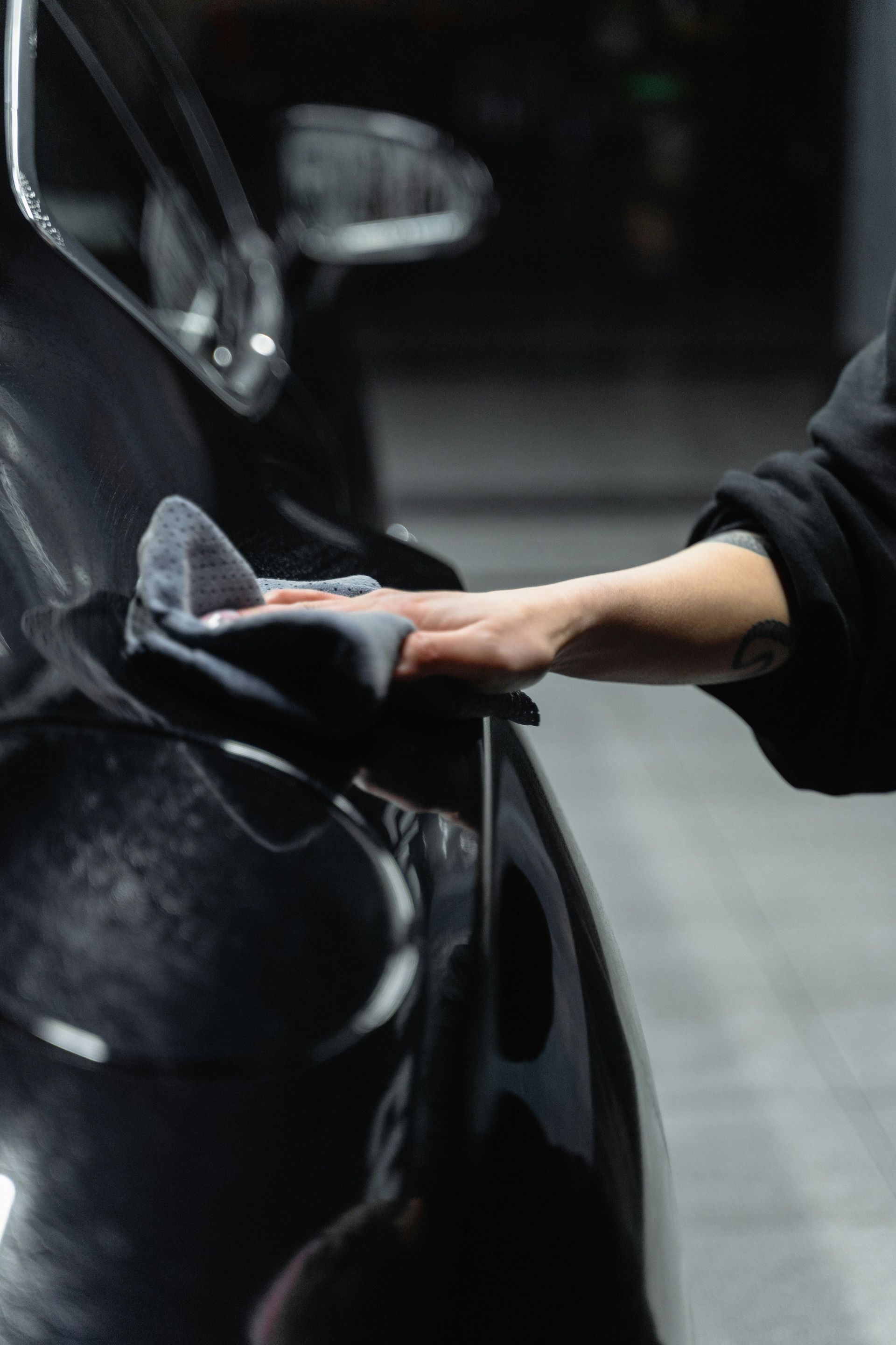 Hand wiping a black car door with a gray cloth in a dark garage