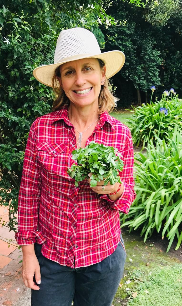 Mujer con sombrero y camisa a cuadros sosteniendo un ramo de hierbas de hojas verdes al aire libre.