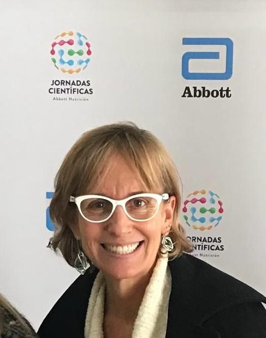 Mujer con gafas blancas sonríe en una conferencia con el logo de Abbott y 