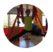 Persona haciendo yoga aéreo, con las piernas bien separadas, suspendida en un columpio de tela roja en un estudio muy iluminado.