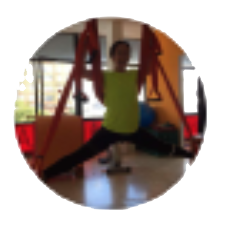 Persona haciendo yoga aéreo, con las piernas bien separadas, suspendida en un columpio de tela roja en un estudio muy iluminado.