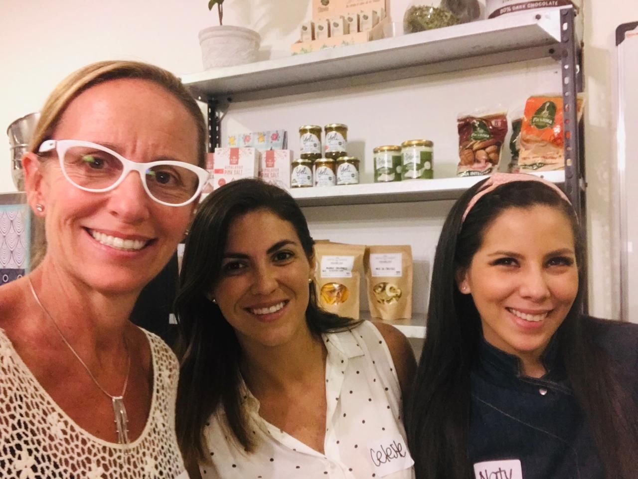 Tres mujeres sonriendo a la cámara frente a estantes de productos alimenticios.
