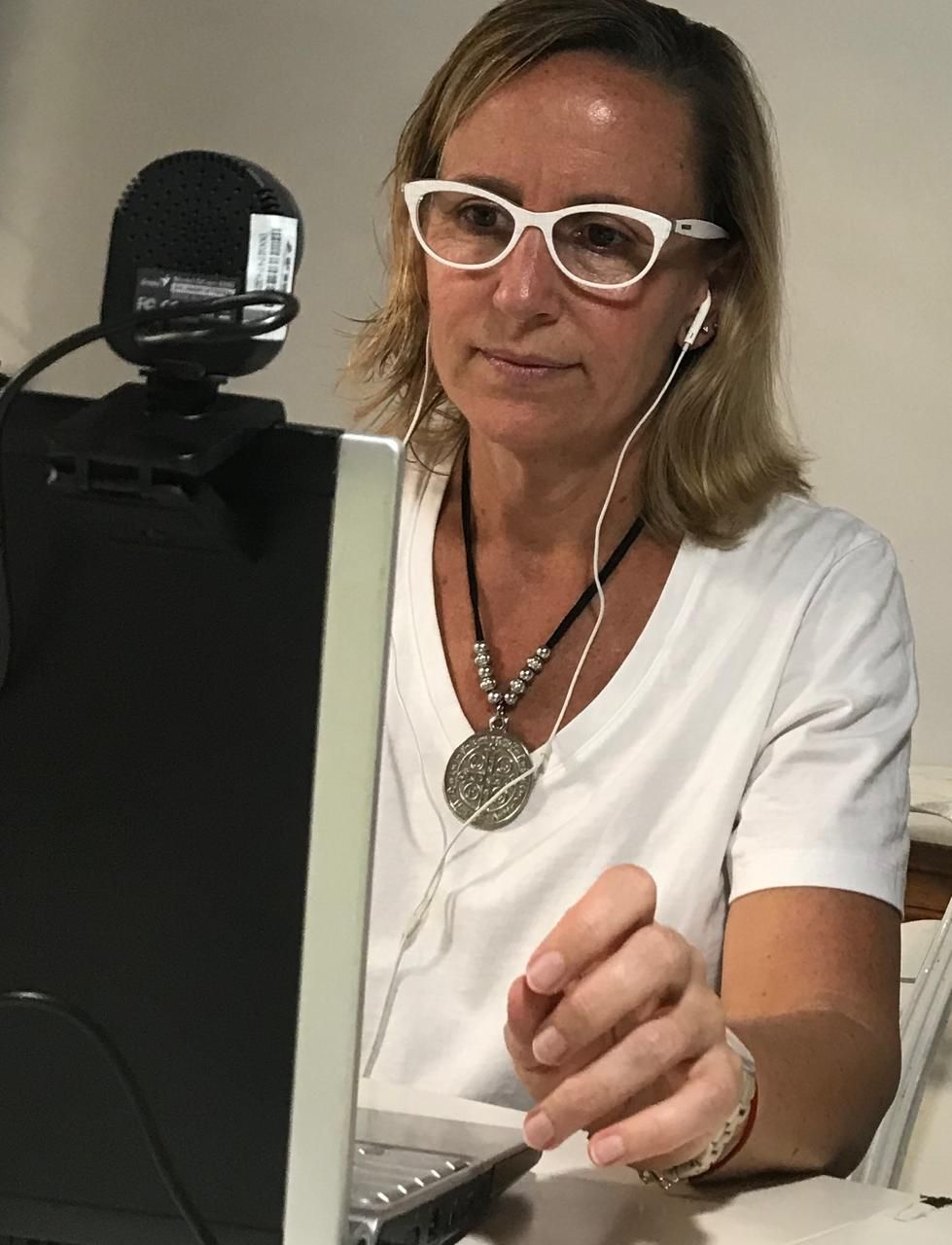 Mujer con gafas y auriculares, mirando una computadora portátil con una cámara web conectada; en el interior.