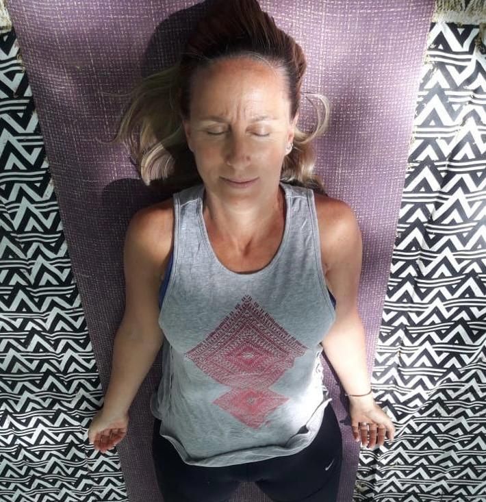Mujer tumbada sobre una esterilla de yoga, con los ojos cerrados, en una pose relajada.
