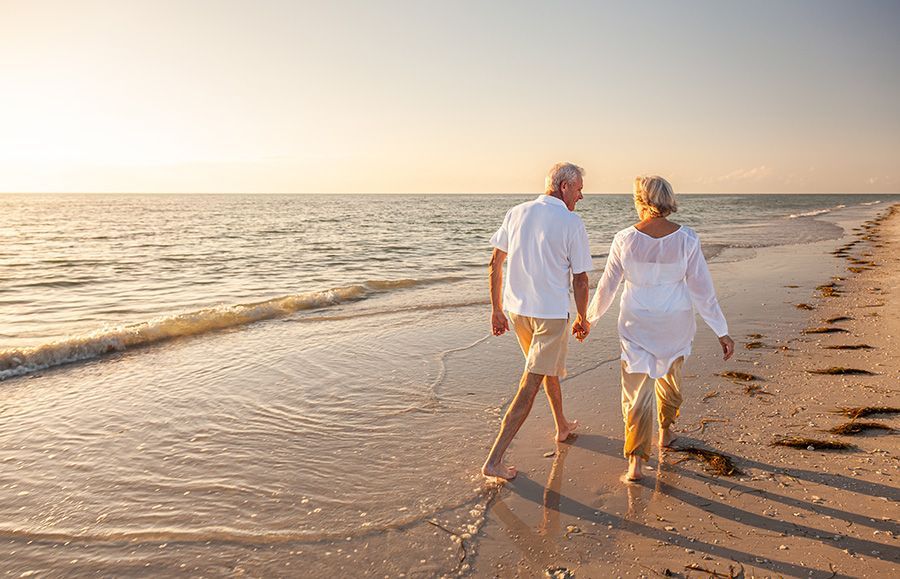 Couple holding hands, walking on a beach at sunset.